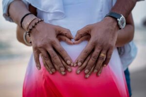 pregnant woman's torso with partner standing behind her, both of their hands on her belly